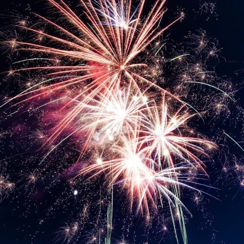 New Year’s Eve fireworks bursting over a European city at night, with bright red, white, and gold explosions filling the dark sky during the city’s celebrations