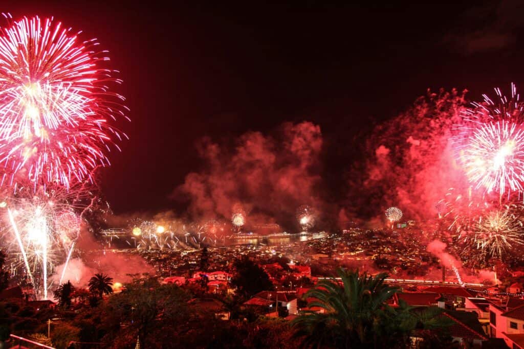 New Year’s Eve fireworks exploding over Funchal, Madeira, with red-lit sky, bursts of colour across the harbour, and the city glowing below at night
