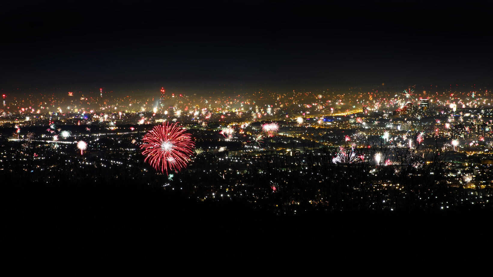 New Year’s Eve fireworks bursting over Vienna at night, with the city lights spread out below and colourful explosions lighting up the skyline