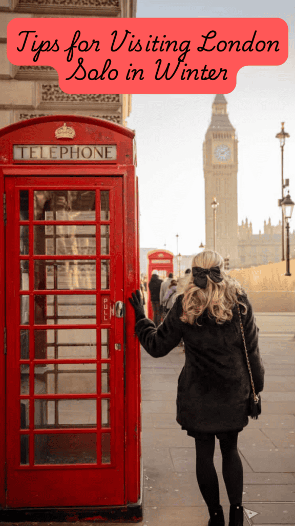 Woman in a black winter coat standing beside a bright red London telephone box with Big Ben in the background, pale winter sky, and soft golden morning light in central London