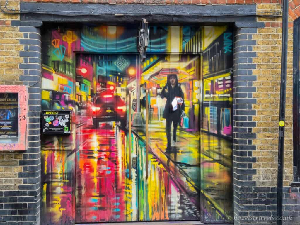 Dan Kitchener street art mural in Shoreditch showing a rain-slicked night street scene with neon signs, car headlights and reflections painted across double doors