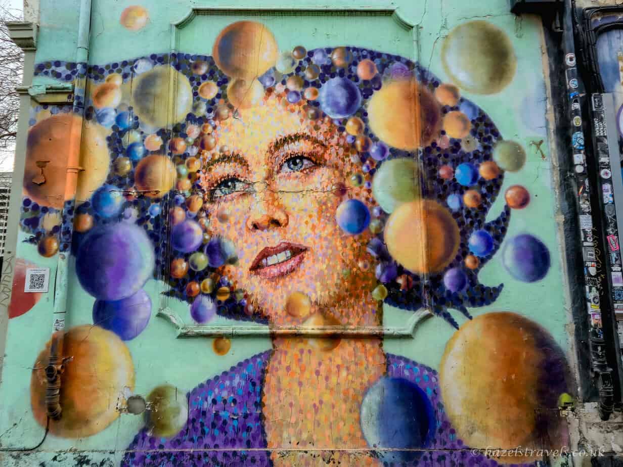 Colourful portrait street art by Jimmy C in Shoreditch, London, depicting a woman’s face formed from layered circular dots in vibrant blues, yellows, and purples