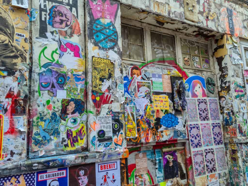 Sticker-covered wall in Shoreditch, London, layered with colourful street art posters, graffiti, political slogans and illustrations on a weathered building facade