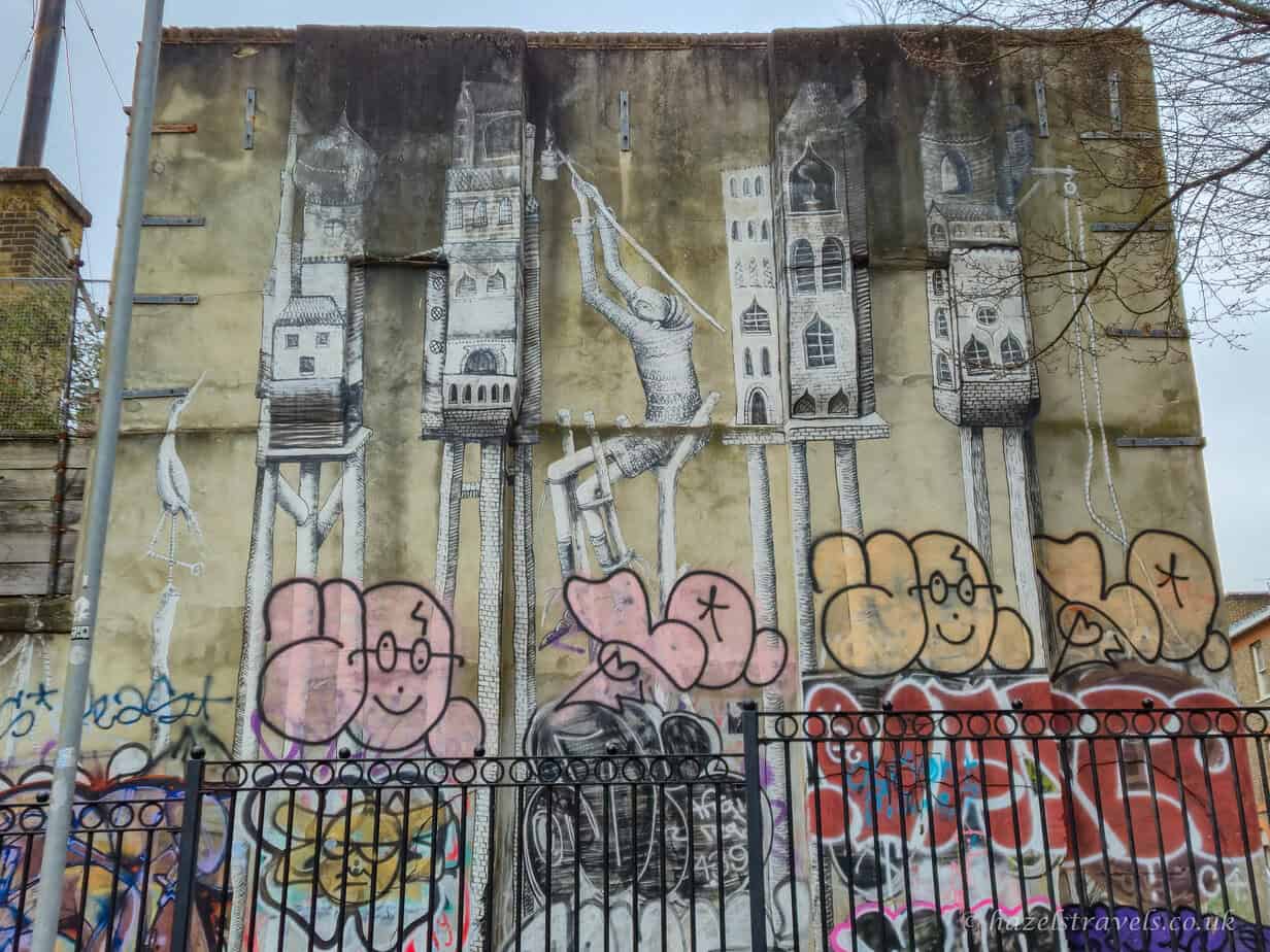 Colourful graffiti artwork painted on an old brick wall with arched recesses, featuring pastel pink and peach bubble lettering against weathered stone and metal railings.
