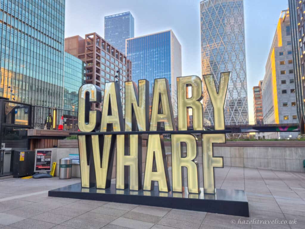 Canary Wharf sign in large illuminated letters set against modern glass skyscrapers in Canary Wharf, London, at golden hour