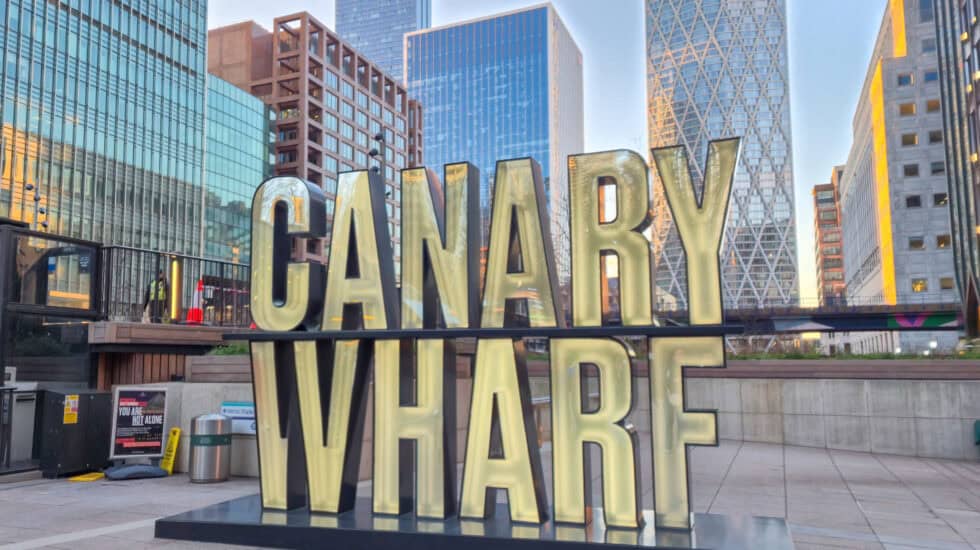 Canary Wharf sign in large illuminated letters set against modern glass skyscrapers in Canary Wharf, London, at golden hour
