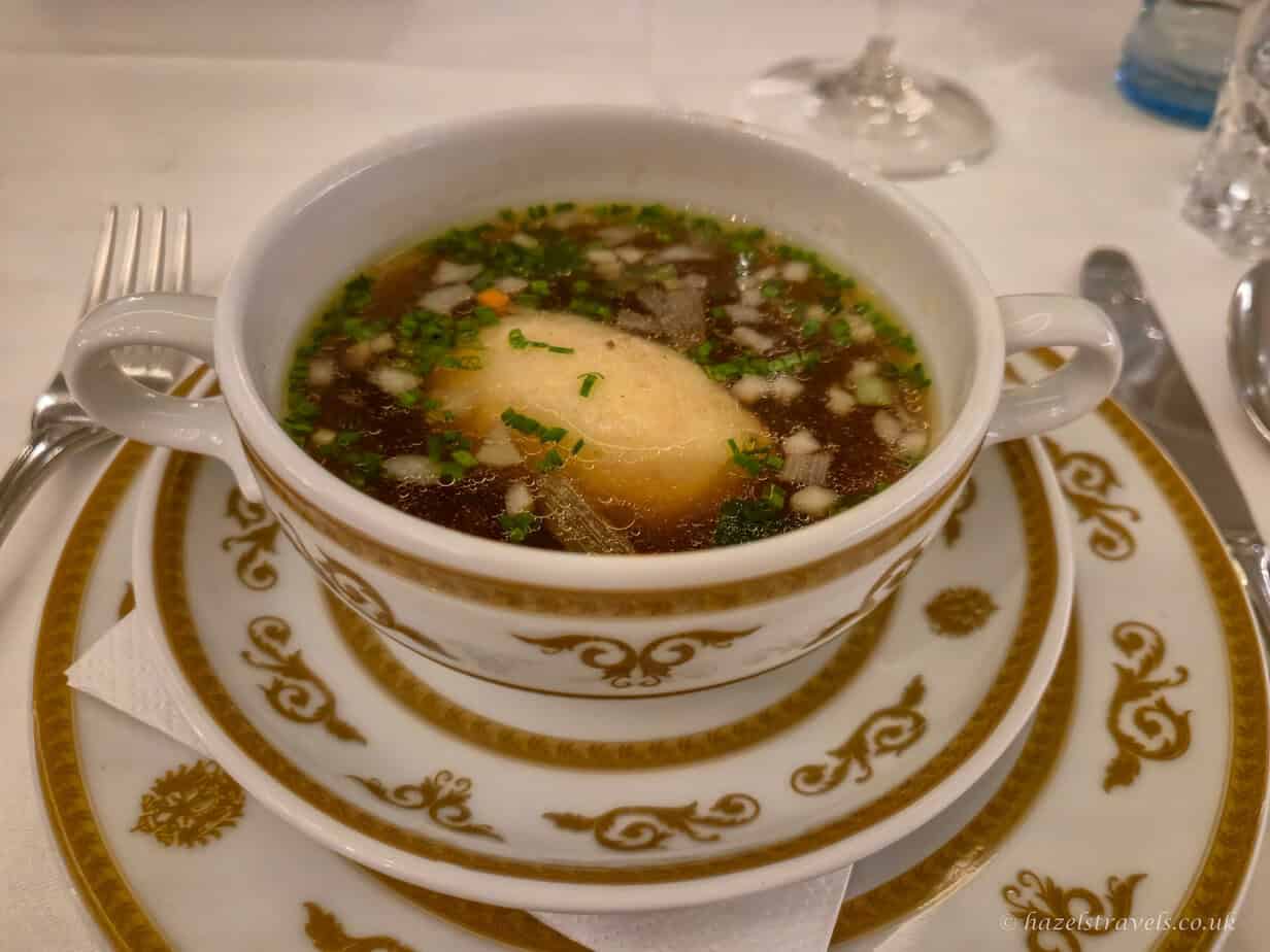 Traditional Viennese food - Tafelspitz broth with semolina dumpling and chives served in a decorative porcelain bowl.