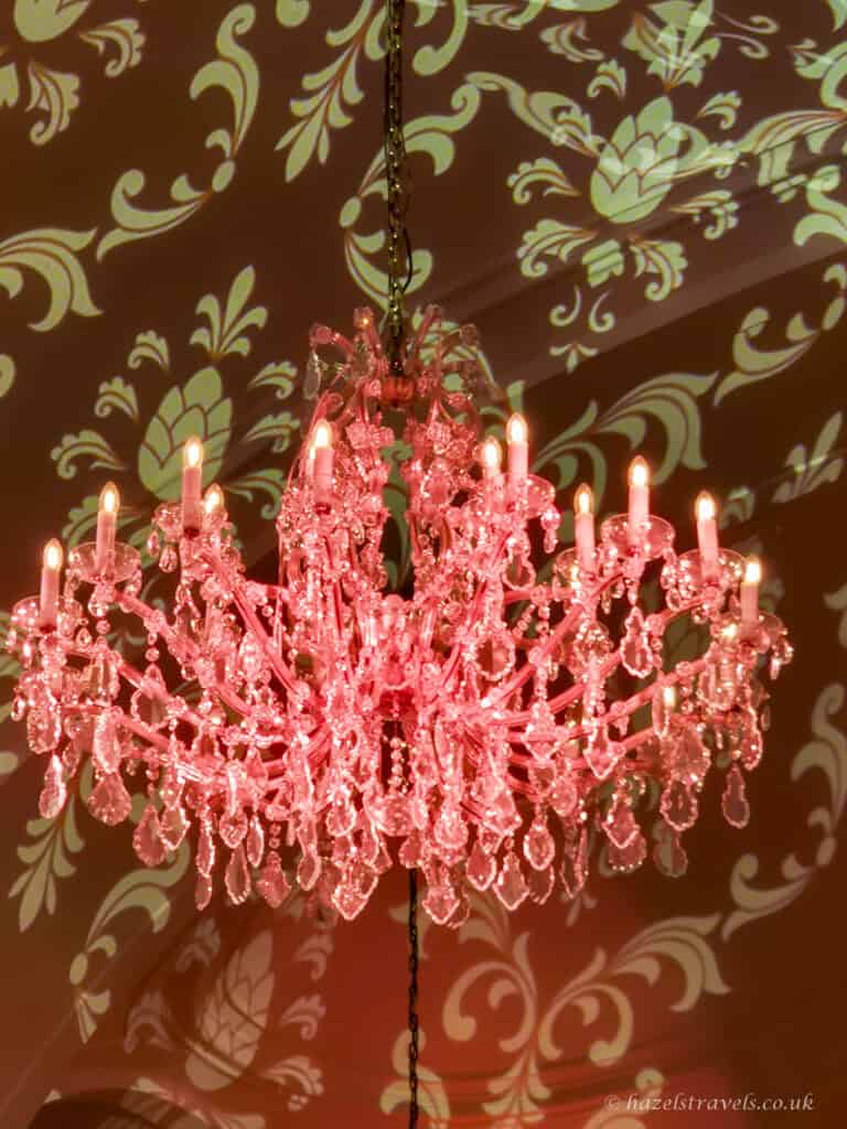 Pink crystal chandelier glowing beneath projected gold floral patterns at the Orangery, Schönbrunn Palace, Vienna