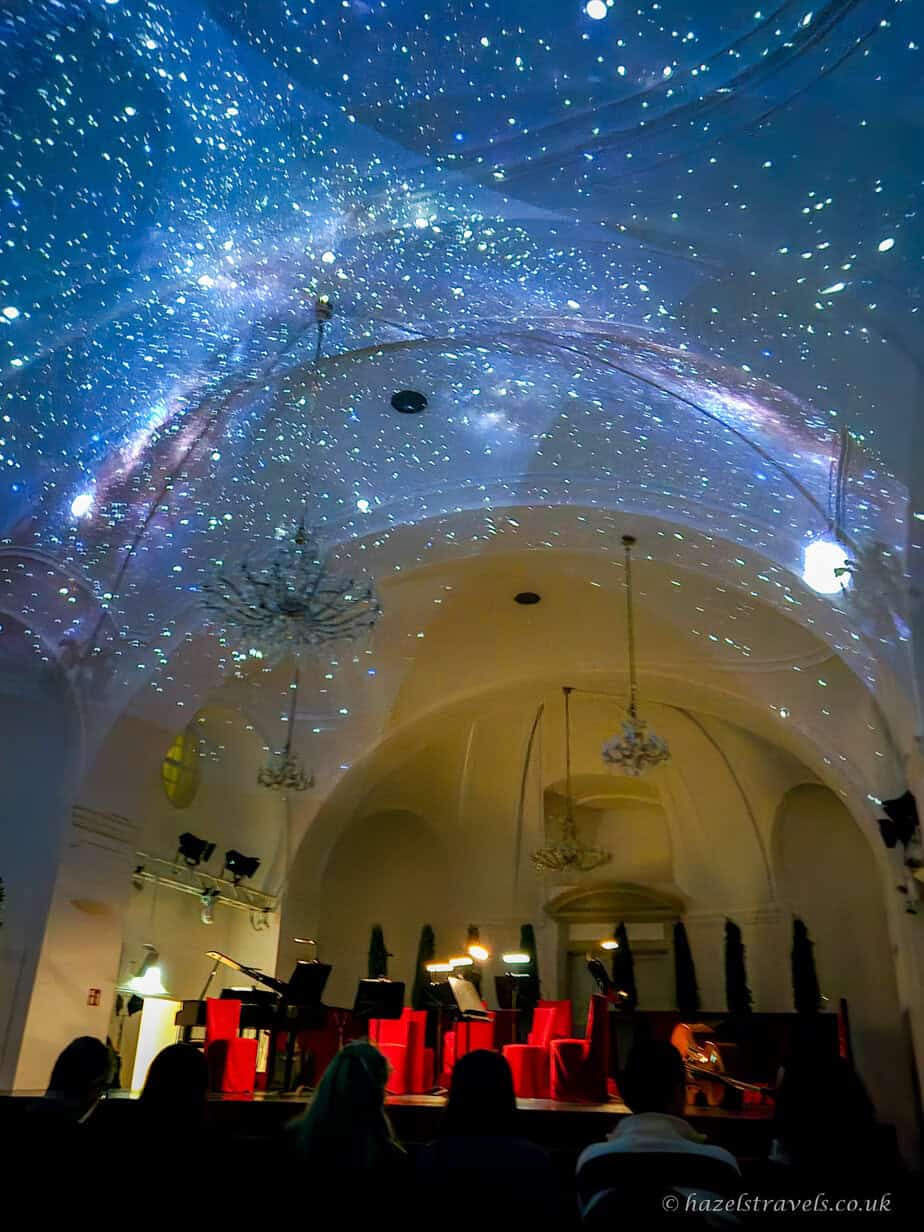 Orangery at Schönbrunn Palace in Vienna lit with blue, starry light projections across the vaulted ceiling and crystal chandeliers before a Mozart concert