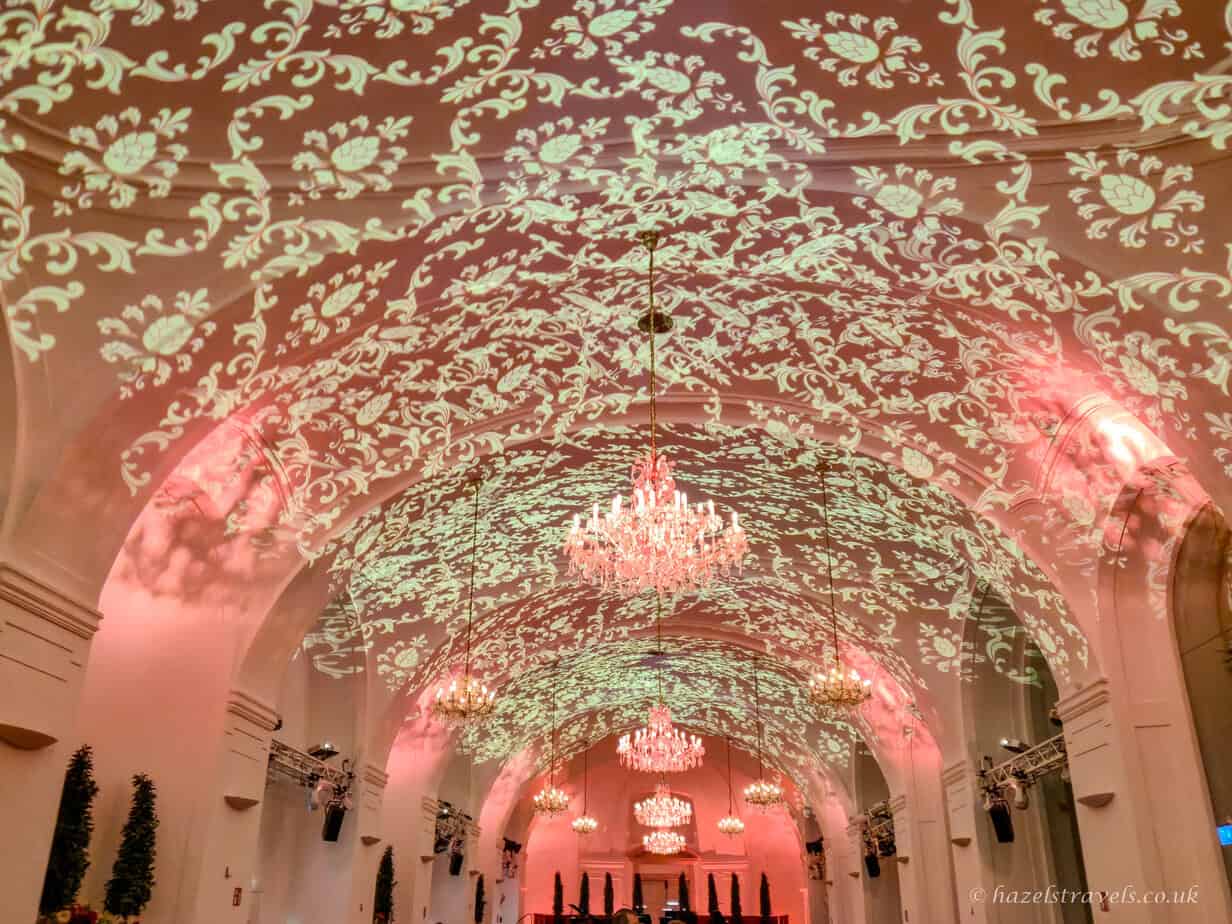 Vaulted ceiling with ornate floral light projections and crystal chandeliers inside the Orangery at Schönbrunn Palace before a Mozart concert, Vienna