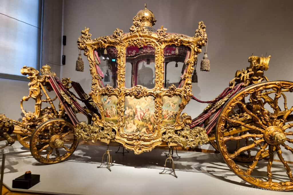 Ornate gilded imperial carriage on display at the Imperial Carriage Museum in Vienna, with intricate gold carvings, painted panels and large decorative wheels