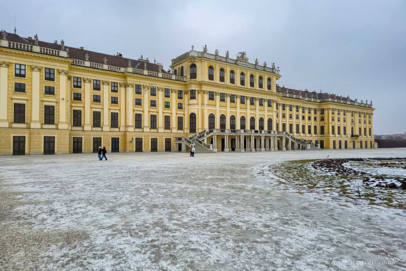 Schönbrunn Palace in Vienna, grand yellow Baroque façade overlooking snow-dusted gardens beneath a grey winter sky