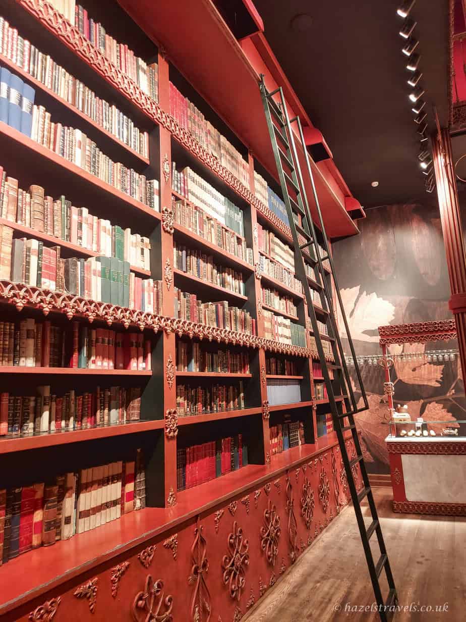 Interior of a wine shop in Porto with tall red shelving stacked with bottles of port wine, creating a narrow aisle under warm lighting.