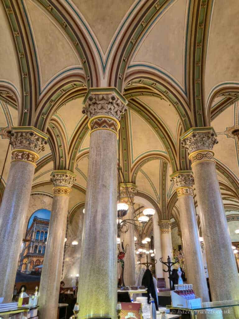 Ornate vaulted ceiling and marble columns inside one of Vienna’s historic coffee houses, with arched detailing and traditional chandeliers.