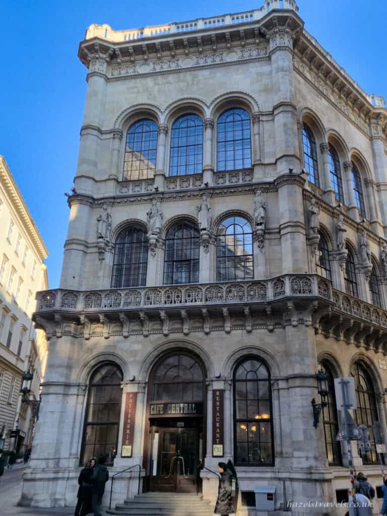 Exterior of Café Central in Vienna, with its ornate historic façade, arched windows, carved stone details, and entrance beneath a clear blue sky.