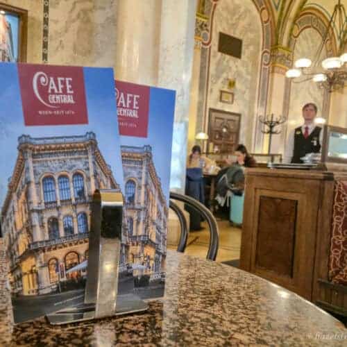 Menu stand on a marble table inside Café Central, one of the most famous Vienna coffee houses, with ornate ceilings and traditional interior in the background.