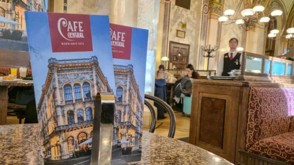 Menu stand on a marble table inside Café Central, one of the most famous Vienna coffee houses, with ornate ceilings and traditional interior in the background.