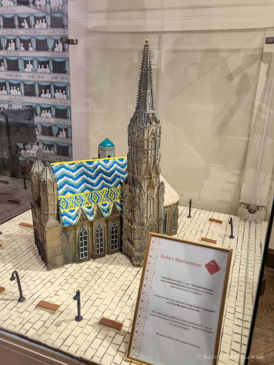 Detailed cake model of St Stephen’s Cathedral displayed inside a glass case at Café Sluka, featuring the cathedral’s tall spire and patterned tiled roof made entirely from confectionery.