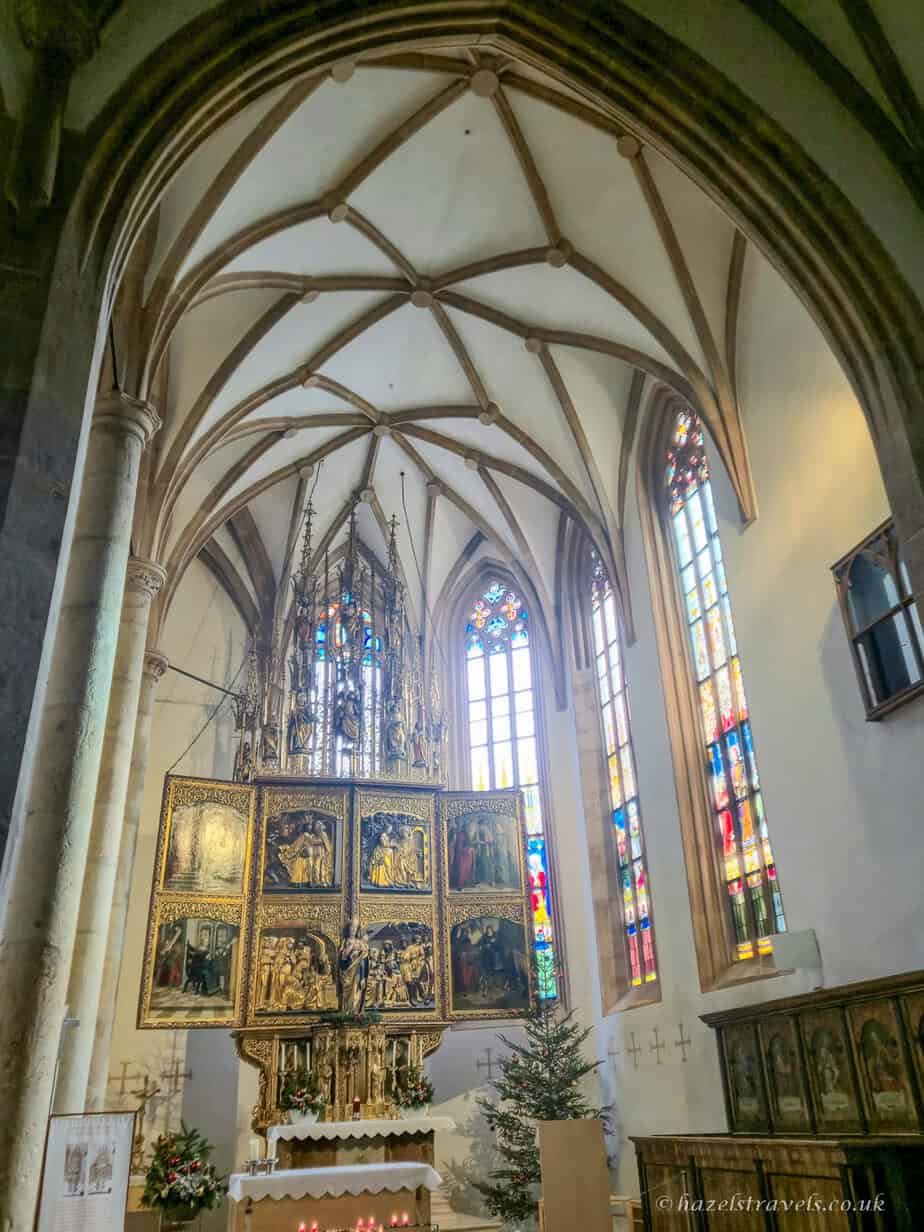 Interior of the Catholic parish church in Hallstatt with vaulted Gothic ceilings, stained glass windows and an ornate golden altarpiece.