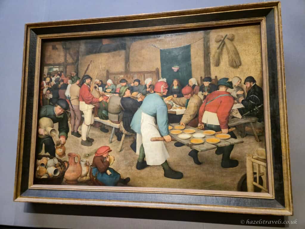 The painting “Peasant Wedding” by Pieter Bruegel the Elder depicting a lively rustic wedding feast with villagers seated at long tables.