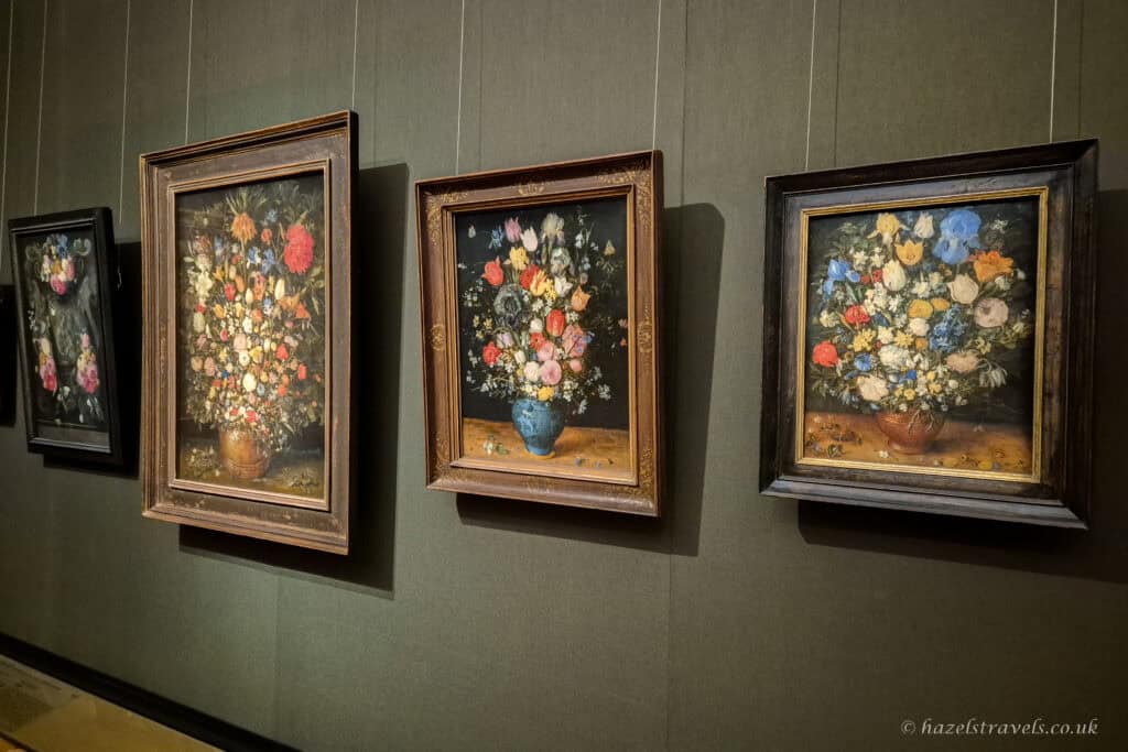 A row of detailed flower still life paintings in ornate frames hanging together in the Kunsthistorisches Museum.