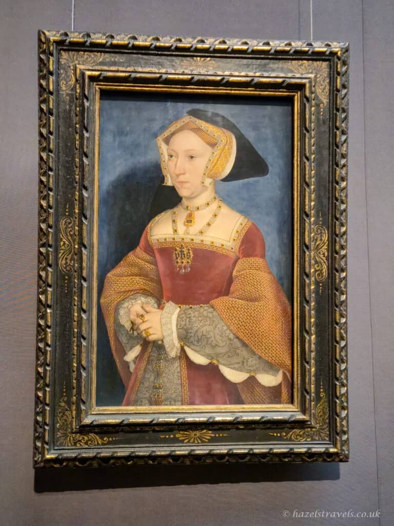 Portrait of Jane Seymour painting by Hans Holbein the Younger, depicting the Tudor queen wearing a red gown, gold jewellery, and traditional Tudor headdress.