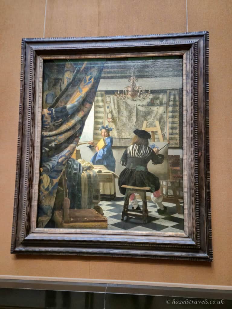 The painting “The Art of Painting” by Johannes Vermeer, depicting an artist painting a model in a detailed studio interior.