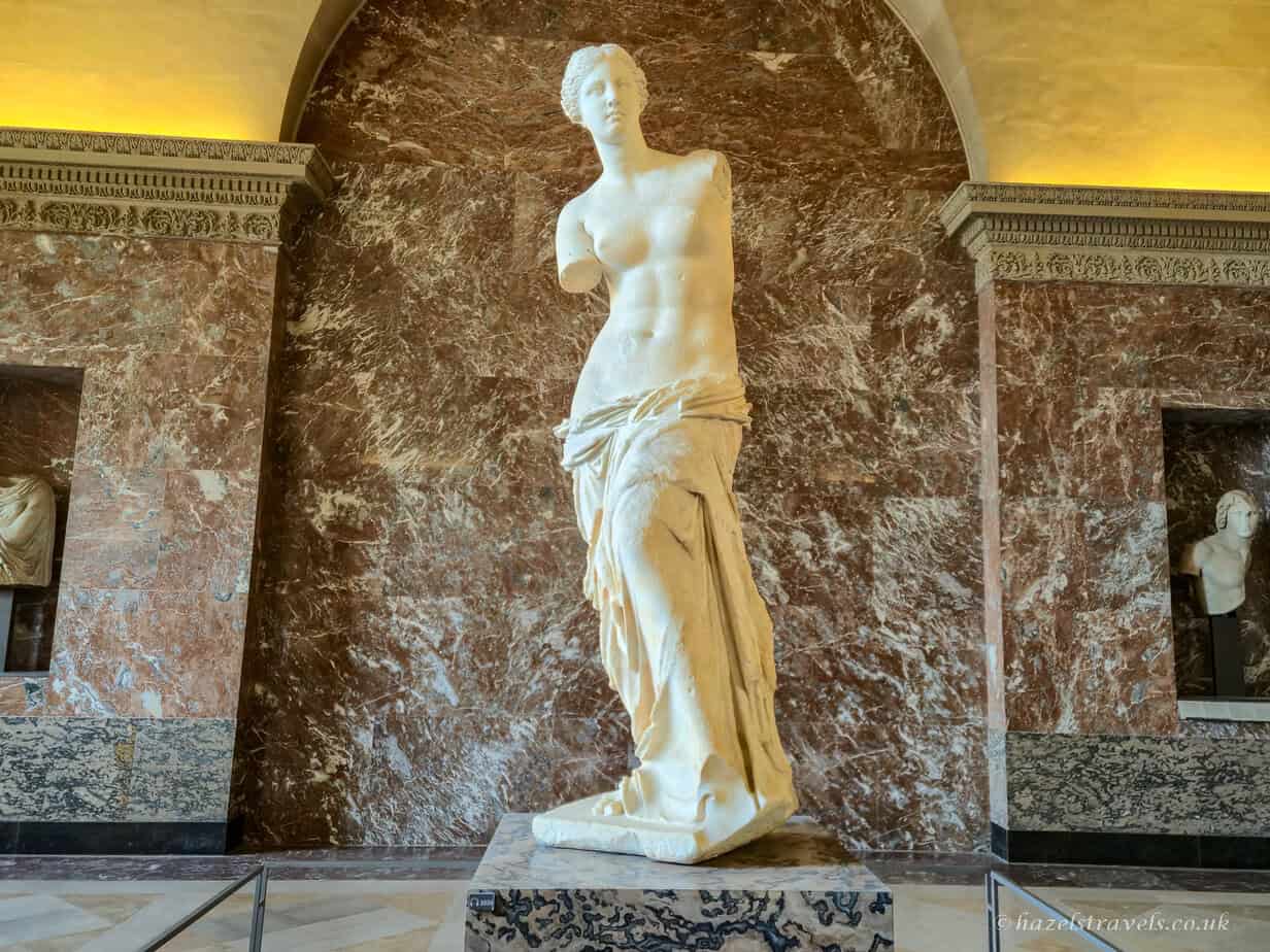 Greek statue, Louvre Museum - Marble sculpture of a classical figure in a brightly lit gallery.