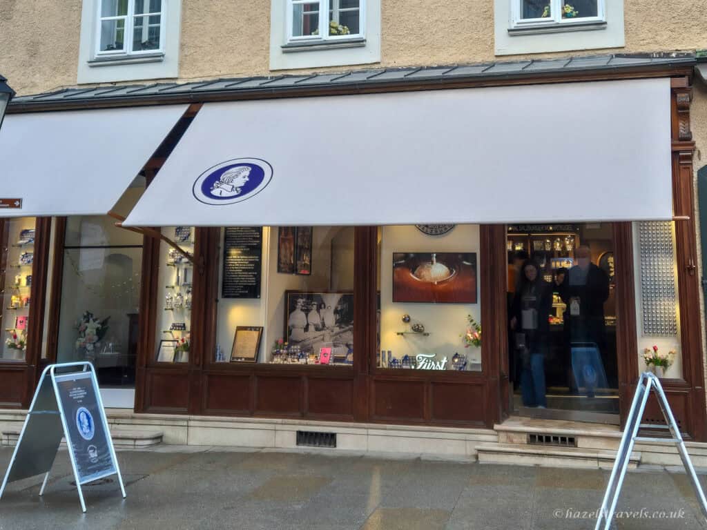 Fürst confectionery shop in Salzburg with cream awning and blue Mozart logo, displaying original Mozartkugel chocolates in the window