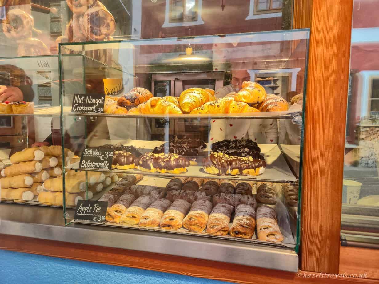 Bakery display case filled with croissants, chocolate pastries, and apple strudel dusted with powdered sugar in a shop window in Hallstatt.