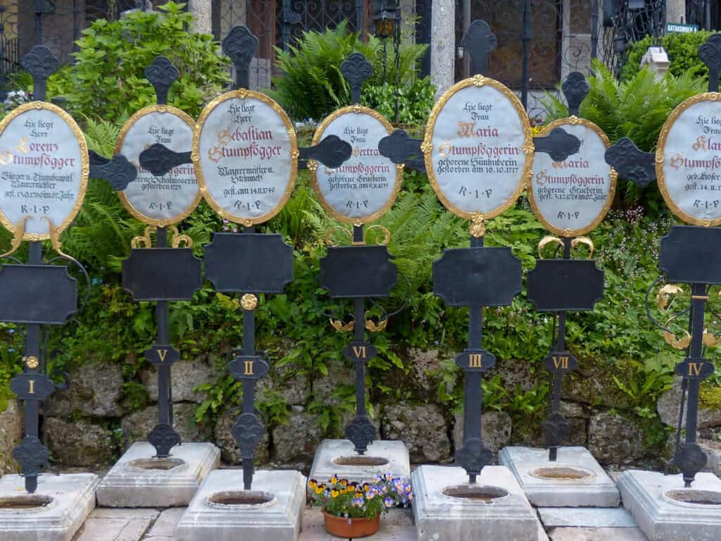 Ornate historic grave markers with gold detailing in St Peterās Cemetery in Salzburg, surrounded by greenery and cloister arches